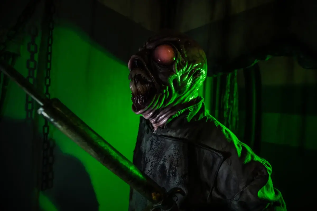 Terrifying creature with glowing red eyes and open mouth illuminated by green light inside Nightmare Cleveland haunted house